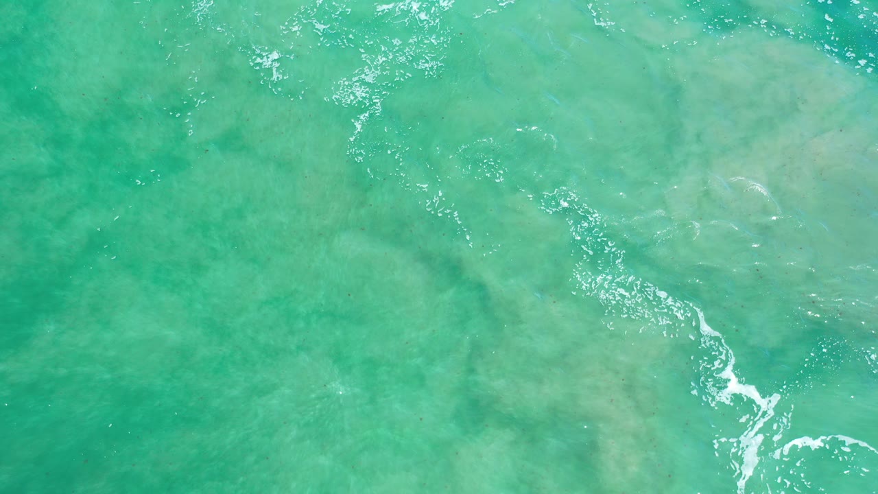 Turquoise Los Cabos seawater fills the frame over pale submerged rock texture, with scattered sun glints and no visible people.