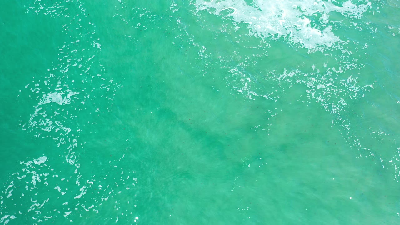 Overhead view of turquoise ocean water in Los Cabos, Mexico, with white foam along the upper edge and no visible people.