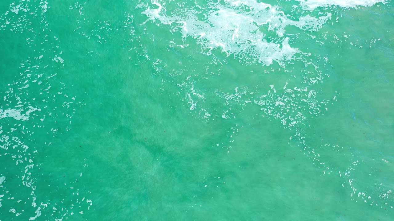Top-down view of turquoise sea in Los Cabos, Mexico, with white foam crossing the upper edge and no visible people.