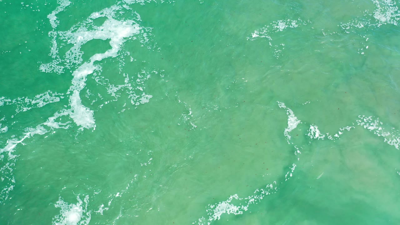 Top-down view of green river water in Los Cabos, Mexico, with white foam near the upper left and lower left, no visible people.