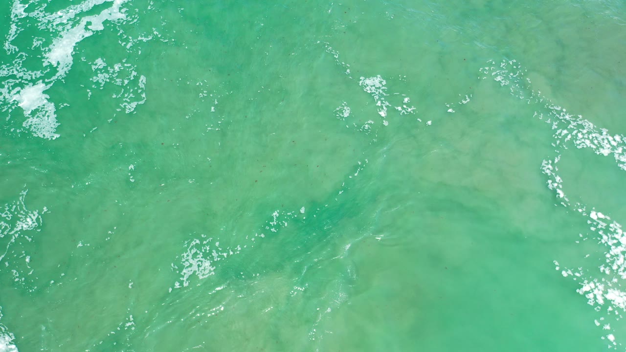 Aerial view of green-turquoise ocean water in Los Cabos, Mexico, with a small white foam patch near the upper left and no visible people.