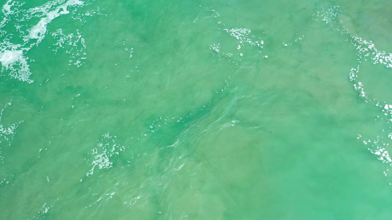 Turquoise ocean surface with bright white foam and faint wave lines.