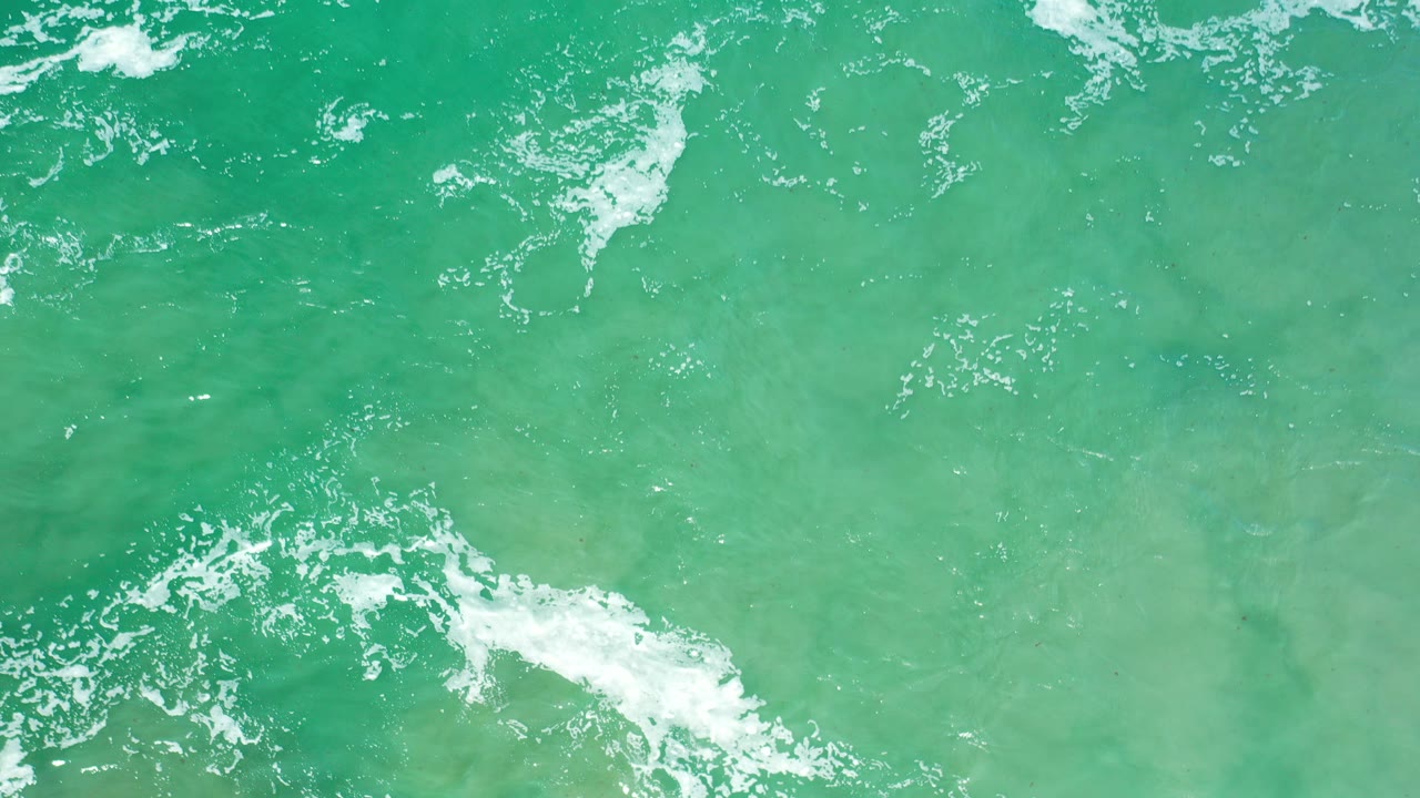 Overhead view of sea-green water in Los Cabos, Mexico, with thin white foam bands near the top and no visible people.