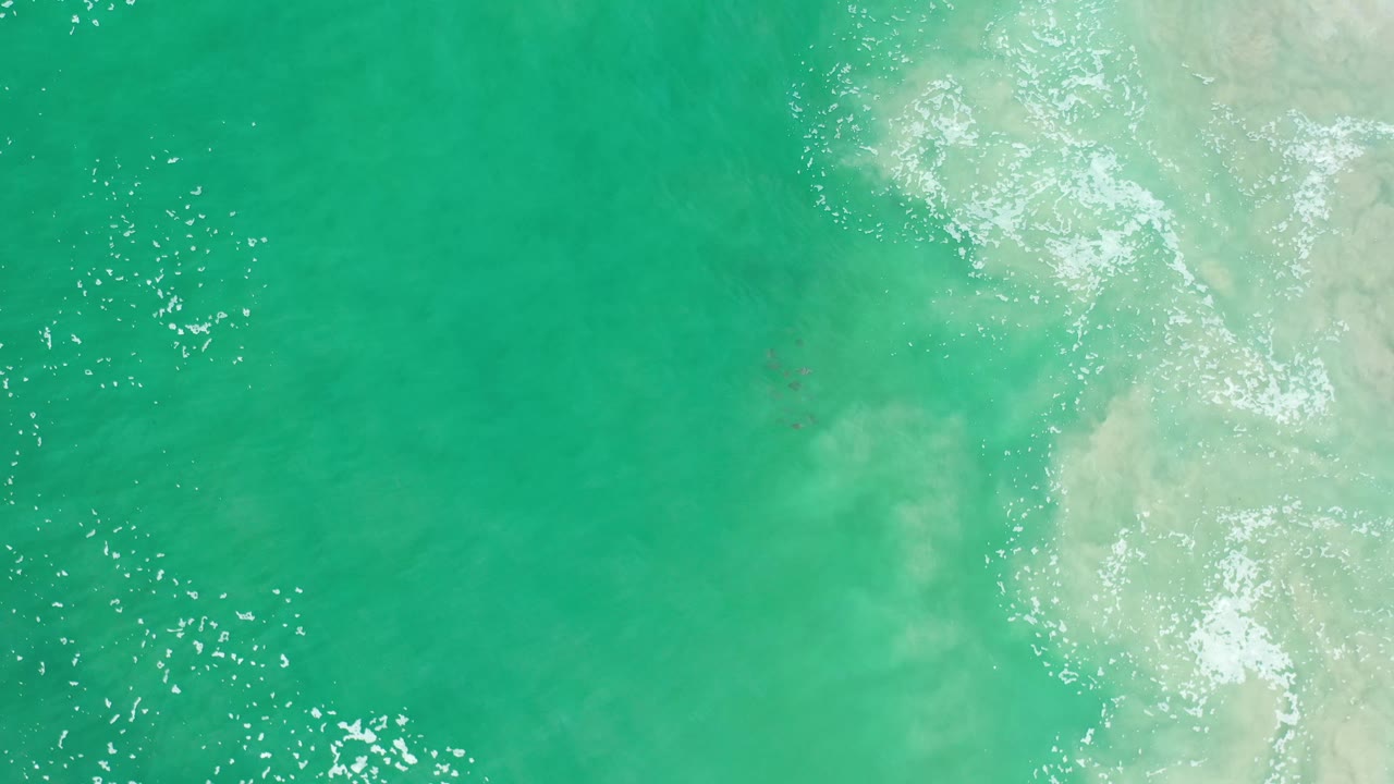 Green sea surface in Los Cabos, Mexico, seen from above with fine ripples, bright reflected highlights, a pale foam band on the right, and no visible people.