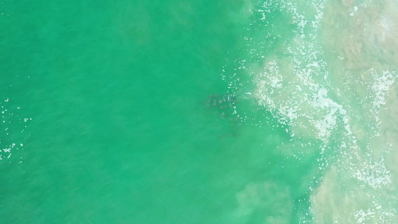Overhead view of turquoise water in Los Cabos, Mexico, with pale surf washing in from the right side and no visible people.