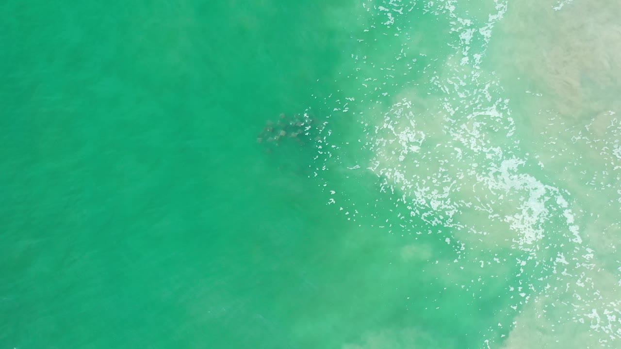Aerial frame of green Los Cabos water with a cluster of white sun sparkle and faint foam along the right edge, with no visible people.