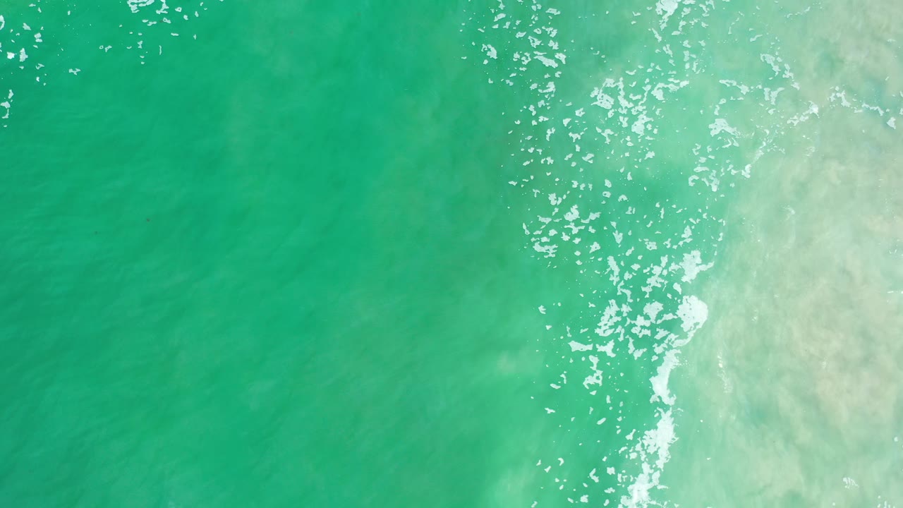 White foam streaks over green ocean near a pale wash.