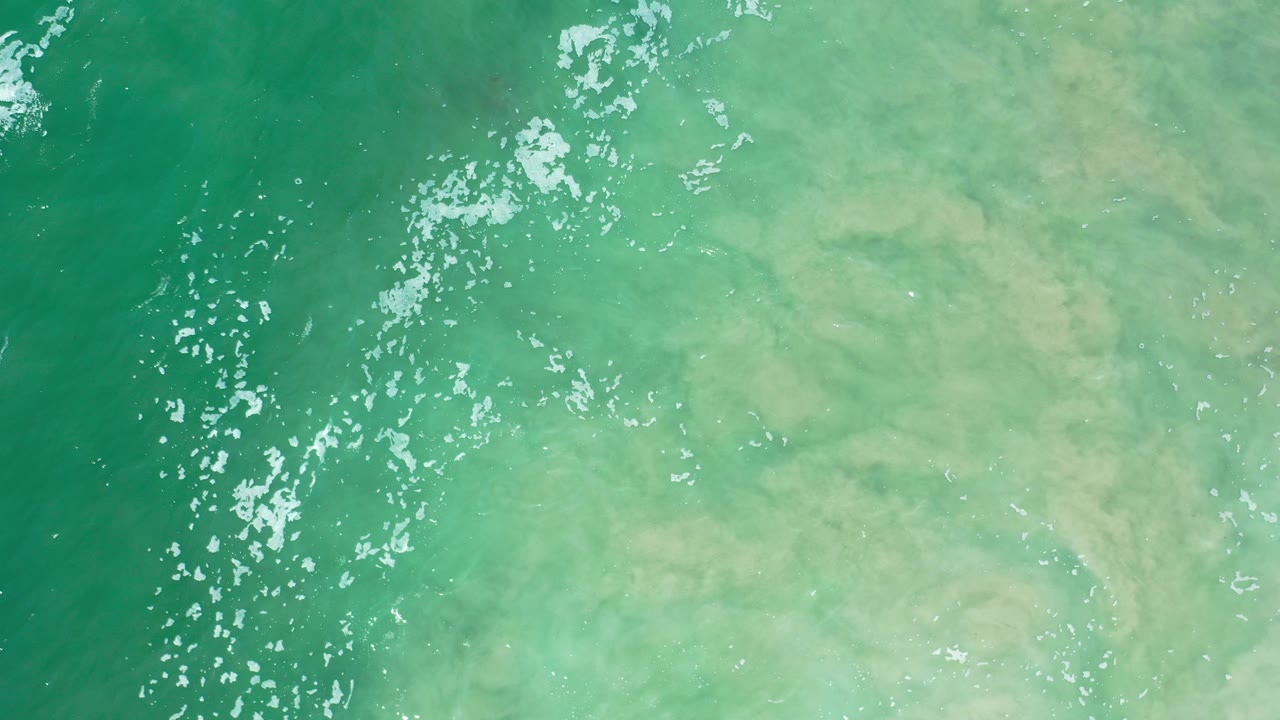Turquoise shallow water over pale sand with sun sparkles.