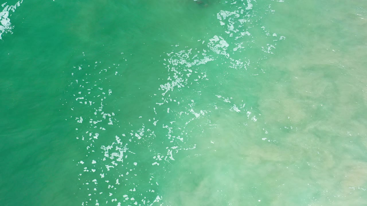 Overhead view of seafoam green ocean water in Los Cabos, Mexico, with white sun glints clustered near the center and no visible people.