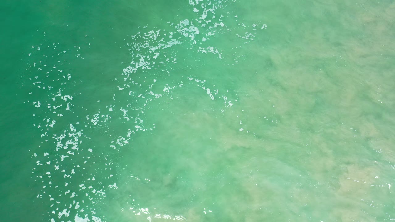 Opening overhead frame of green Los Cabos seawater with scattered white highlights, cloudy pale tones below the surface, and no visible people.