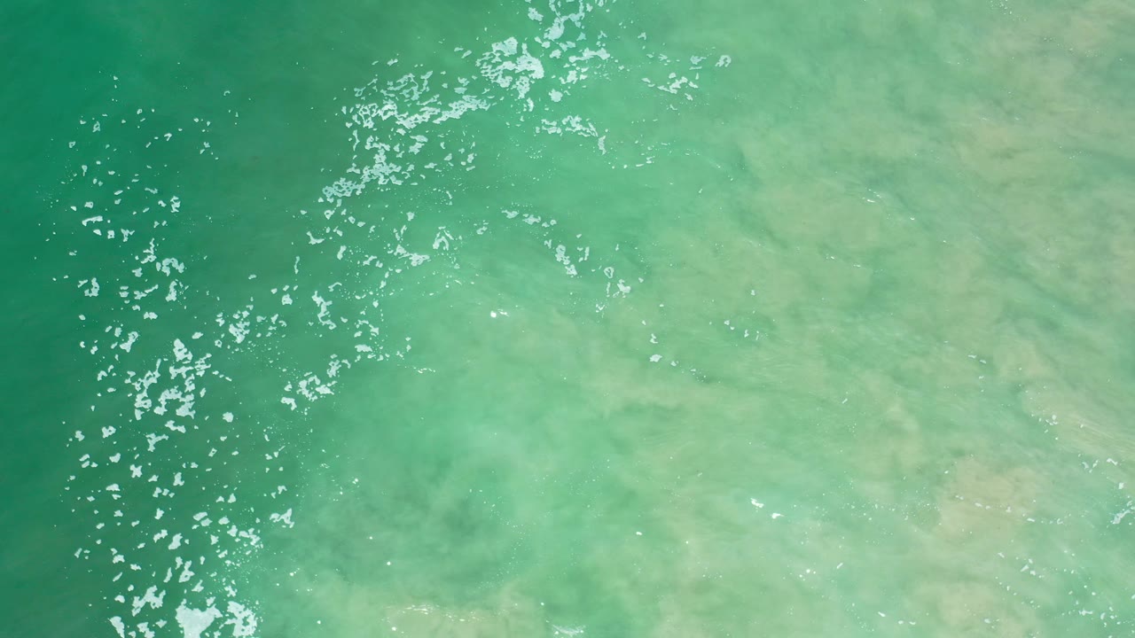 Aerial green water with dense sparkle along the left side and pale sandy color beneath.