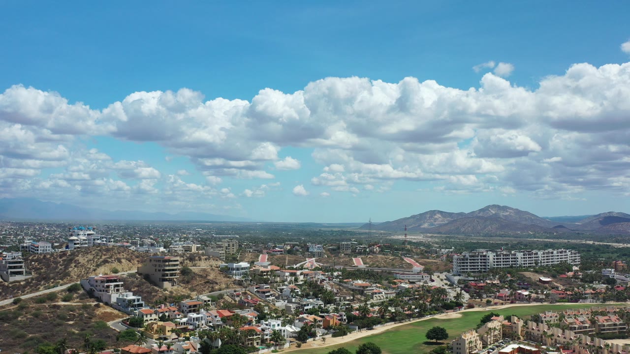 Wide aerial view of city below mountains and large clouds.