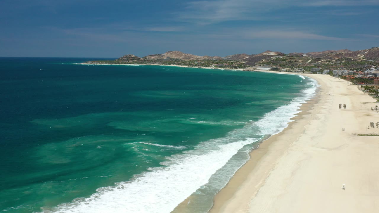 Wide aerial view of a curved beach beside blue-green ocean.