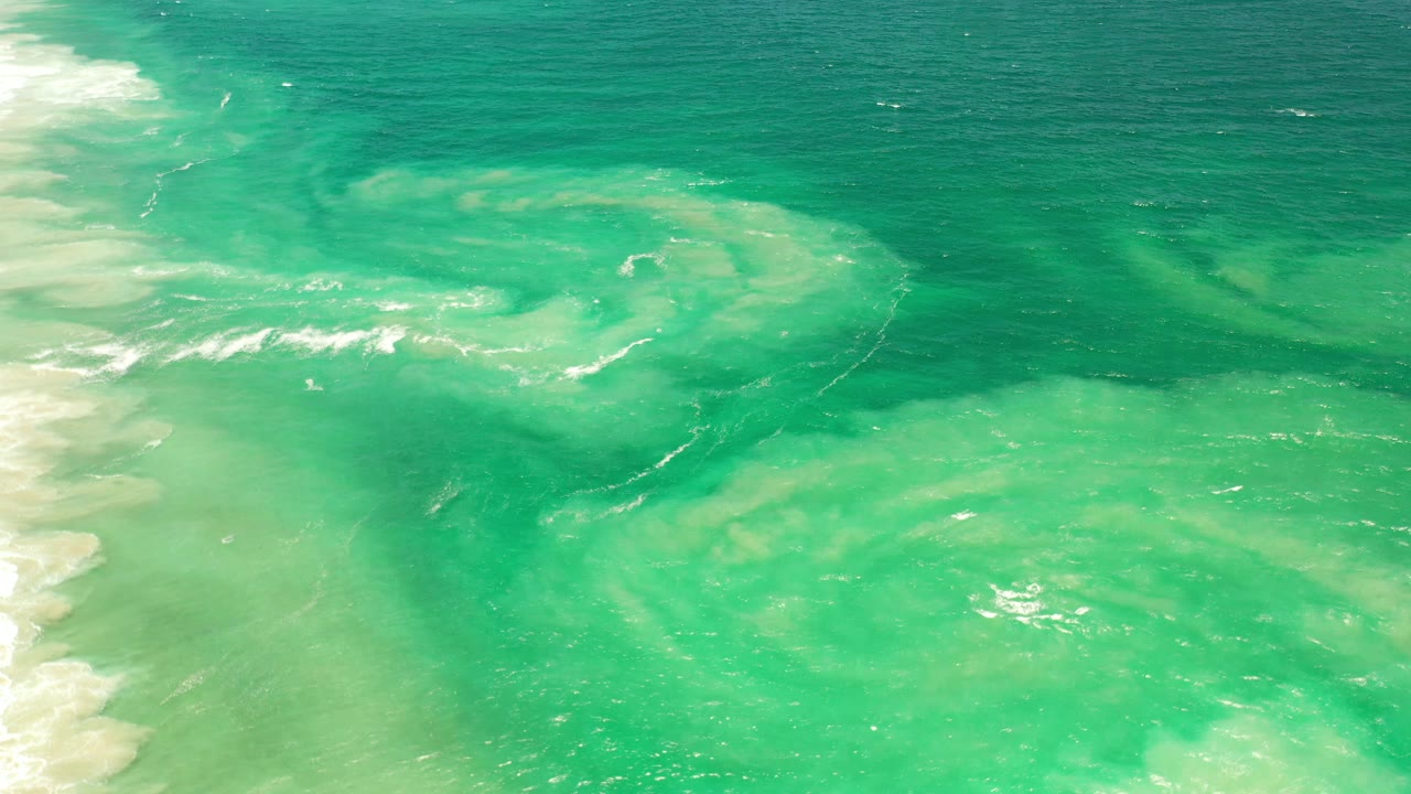 Aerial Los Cabos ocean frame with pale foam bands over turquoise water, darker water along the top, and no visible people.