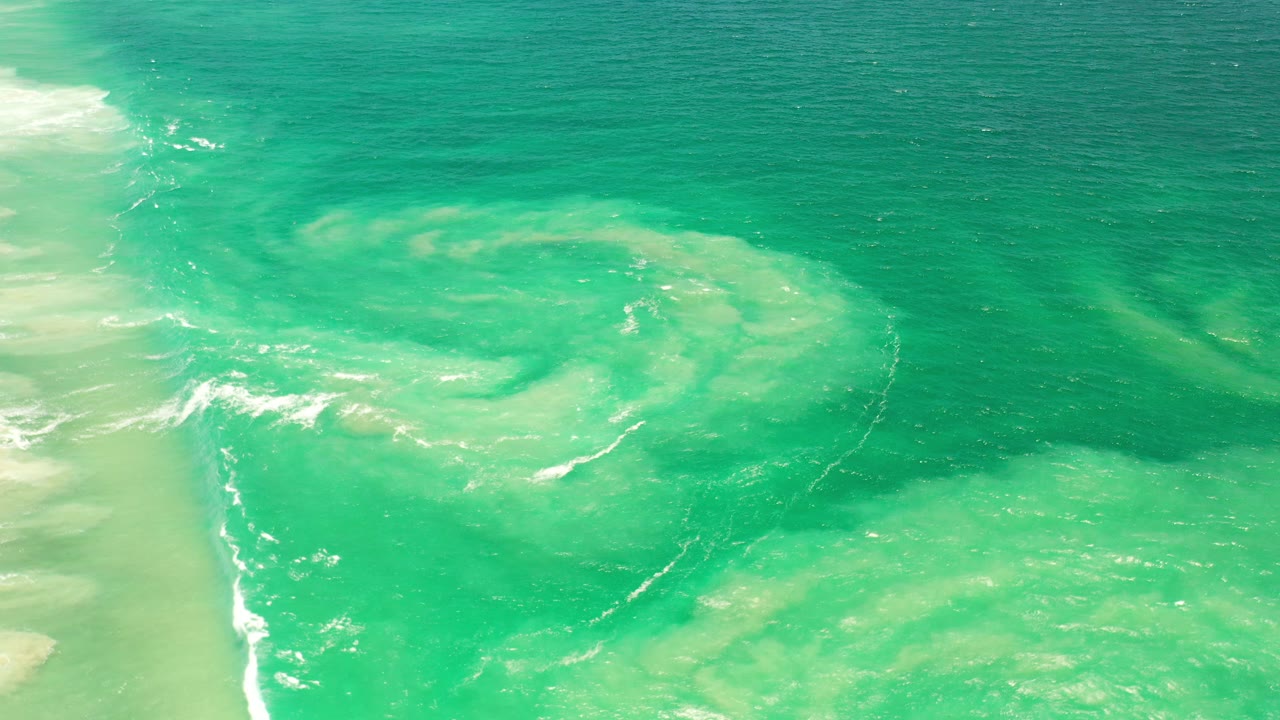 Top-down view of turquoise ocean water and white surf near pale sand.