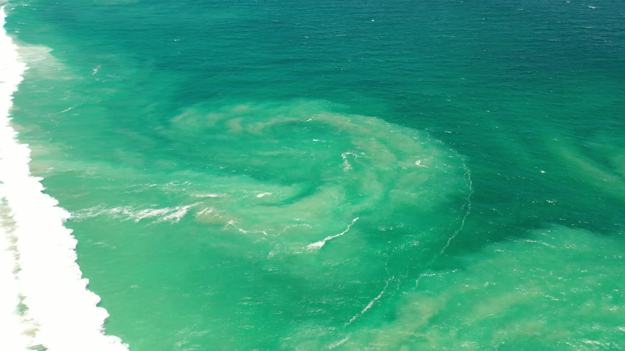 White wave edge beside turquoise water and sandy swirls.
