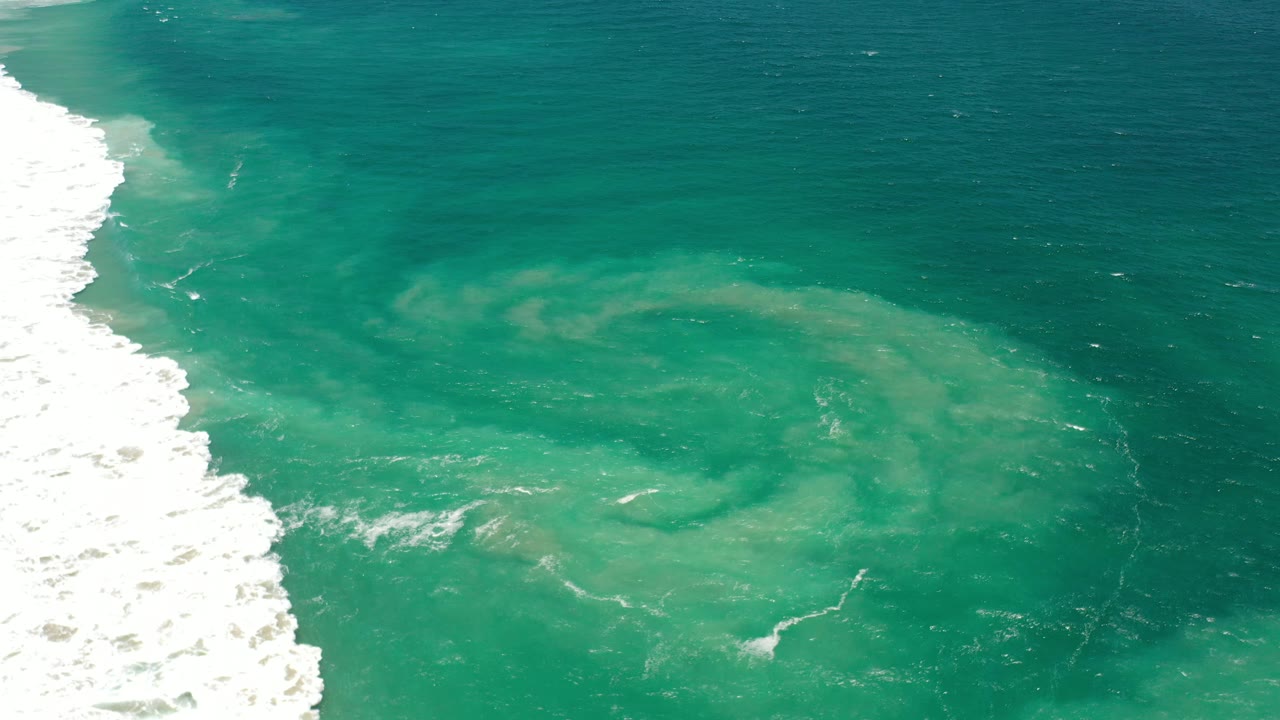 White shore break and green circular water pattern offshore.