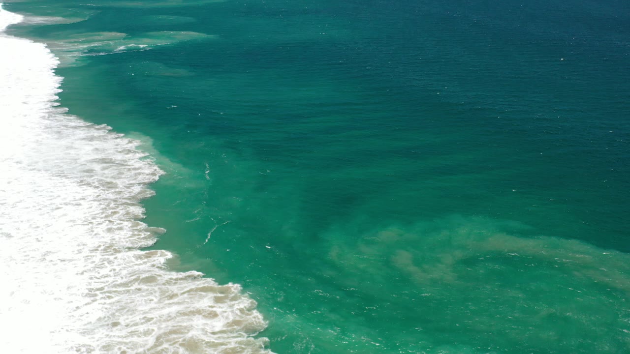 Aerial view of white surf pushing along the left side of green Los Cabos ocean water, with no visible people.