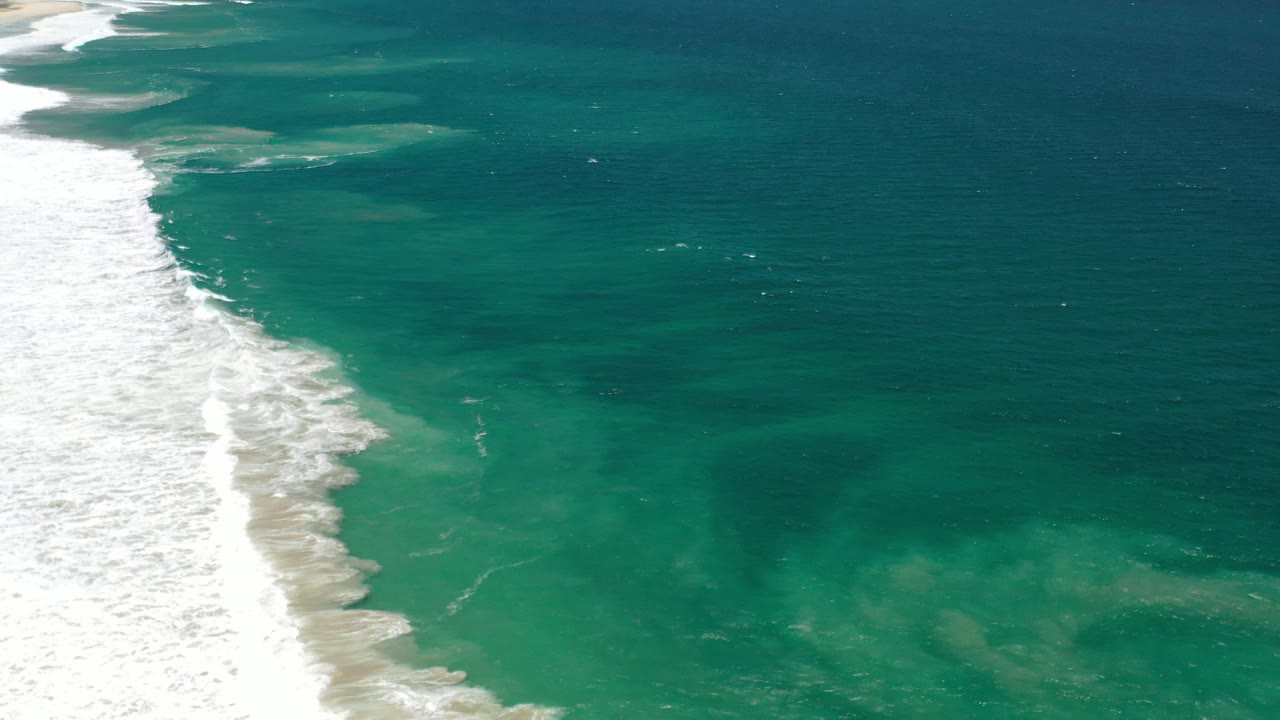 Aerial view of teal ocean and white surf along the shore
