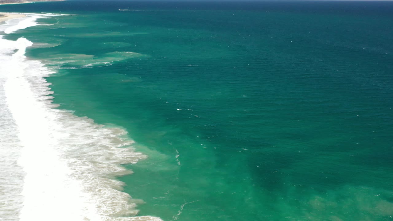 White waves breaking beside turquoise and dark ocean water