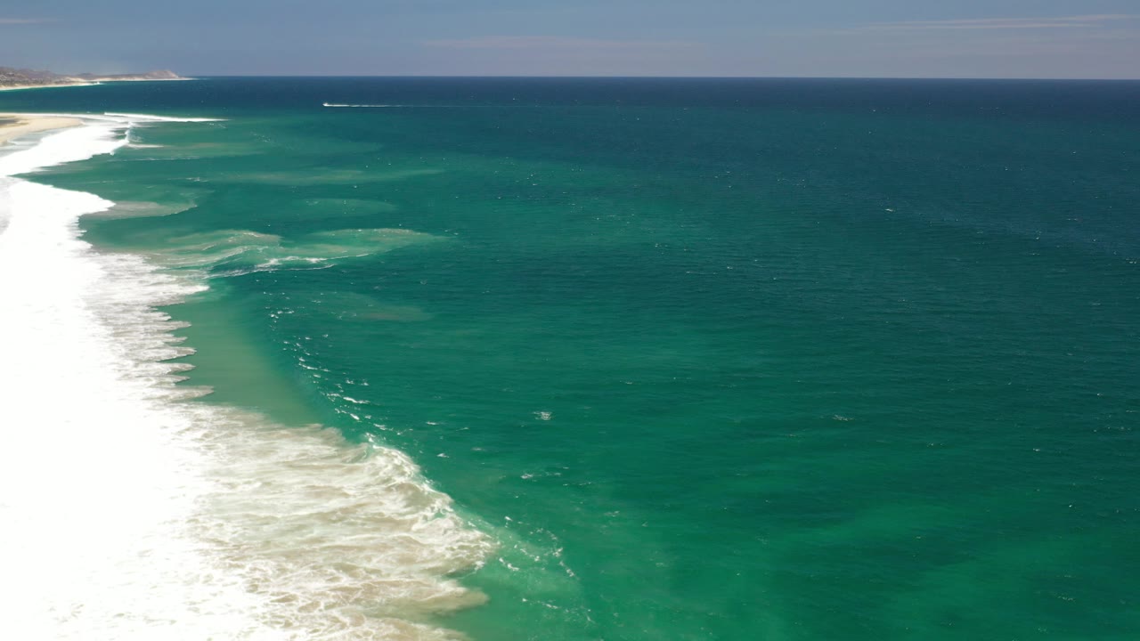 Long beach edge with foamy waves and open ocean.