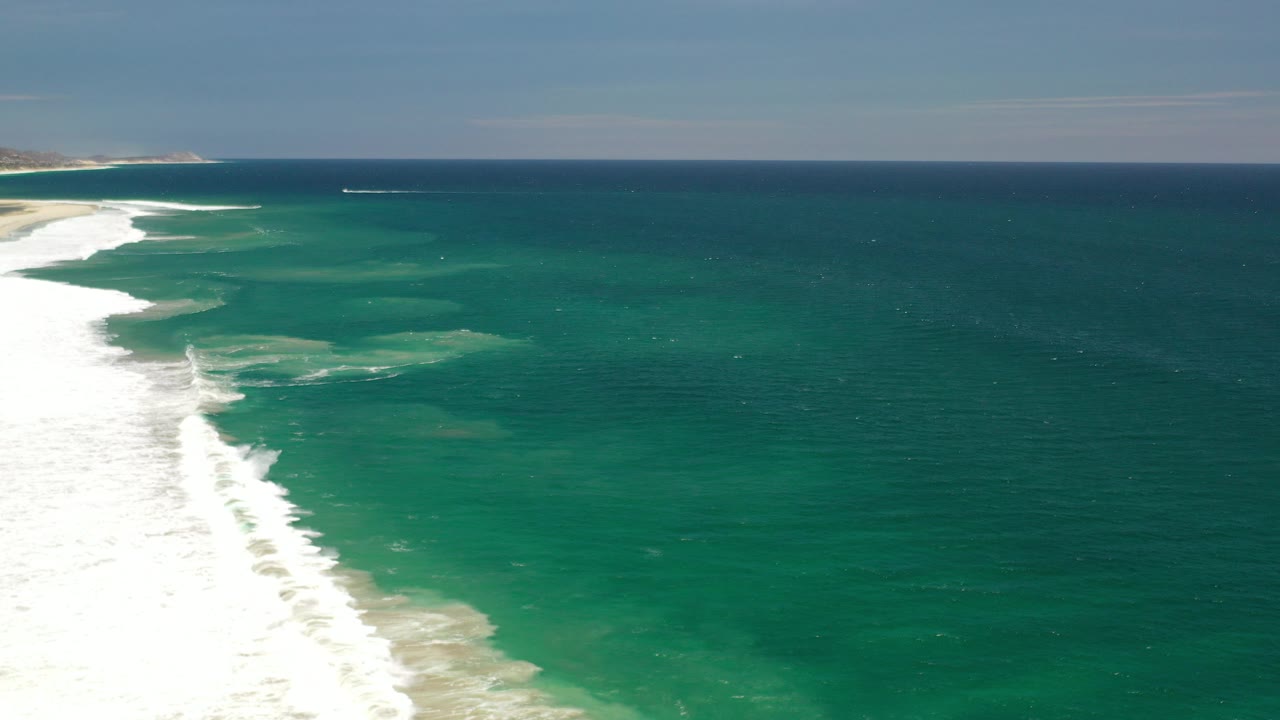Aerial view of surf breaking beside turquoise ocean.
