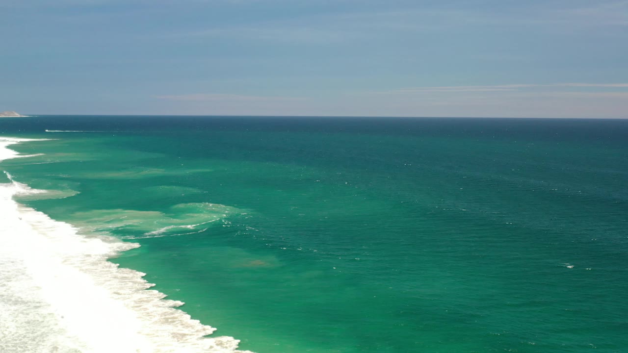 Clear ocean with pale sandbars or shallow patches beneath small waves.