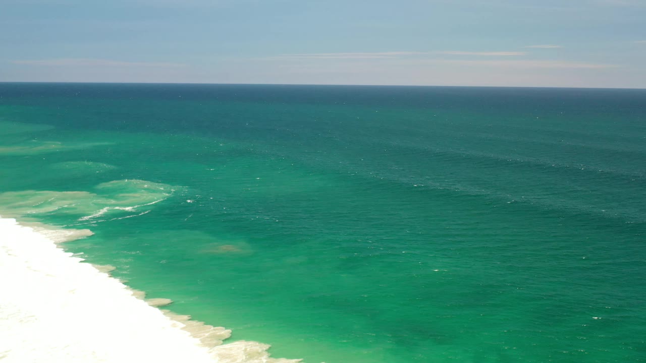 Aerial Los Cabos coastline frame with bright sand entering from the lower left, foamy surf bands near shore, green-blue water offshore, and no visible people.