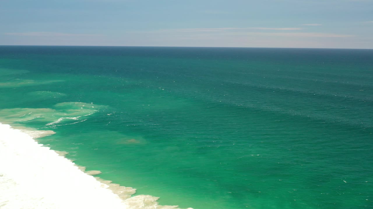 Wide aerial ocean view with beach and surf along the left side of frame.