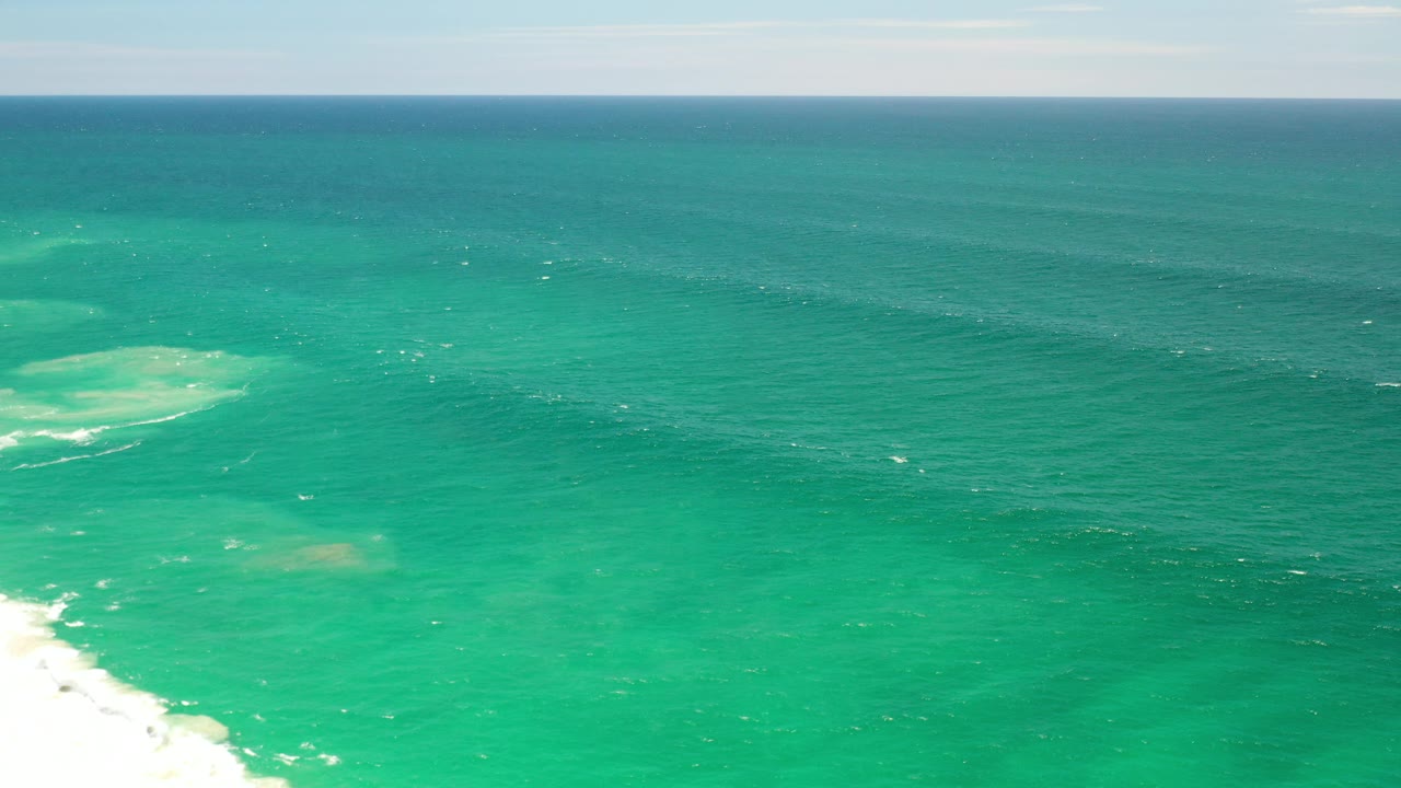 Elevated view of green ocean with horizon and pale surf at the lower left.