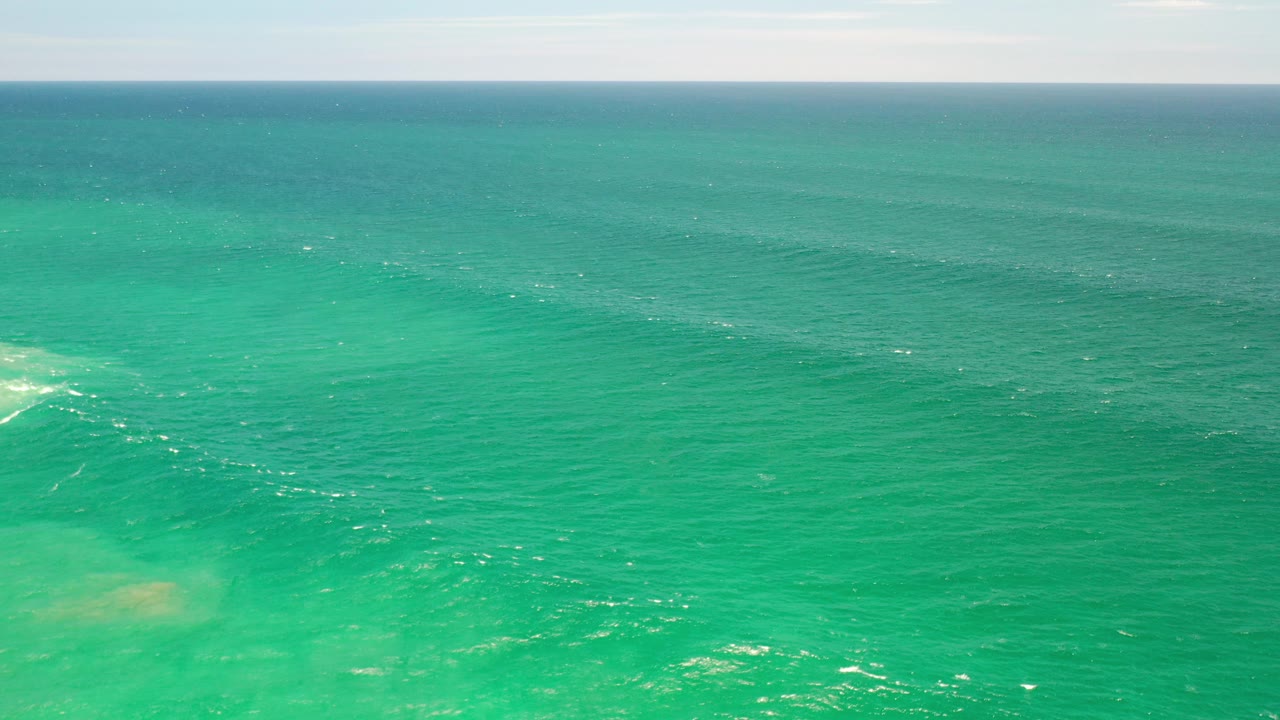 Opening frame of turquoise sea in Los Cabos, Mexico, with a straight horizon, small white ripples, pale underwater patches, and no visible people.