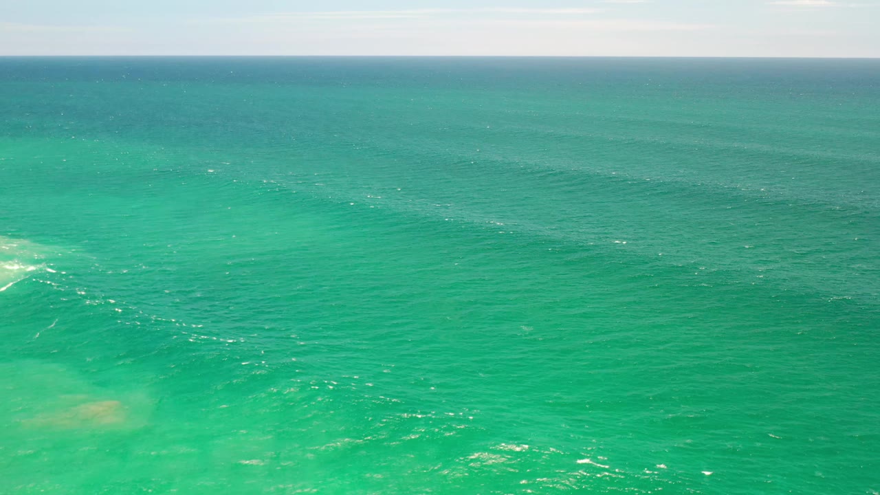 Turquoise-green ocean in Los Cabos, Mexico, with sunlit ripples, a pale submerged patch near the lower frame, a flat horizon, and no visible people.