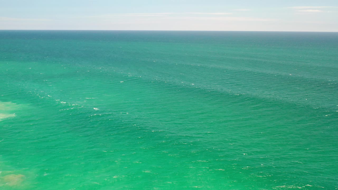 Green ocean water stretches toward a pale horizon in Los Cabos, Mexico, with small white surface flecks and no visible people.