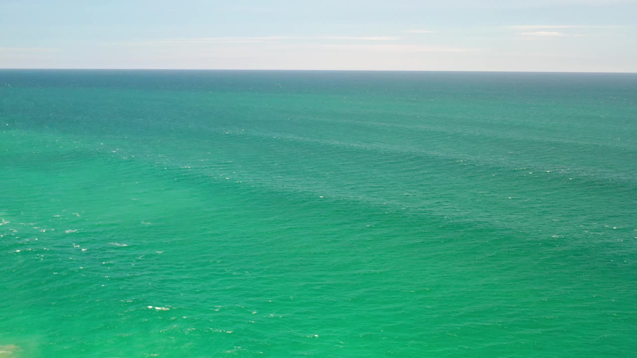 Early frame showing the Los Cabos sea spread across the foreground, with faint white ripples and a narrow strip of pale sky above the horizon, no visible people.