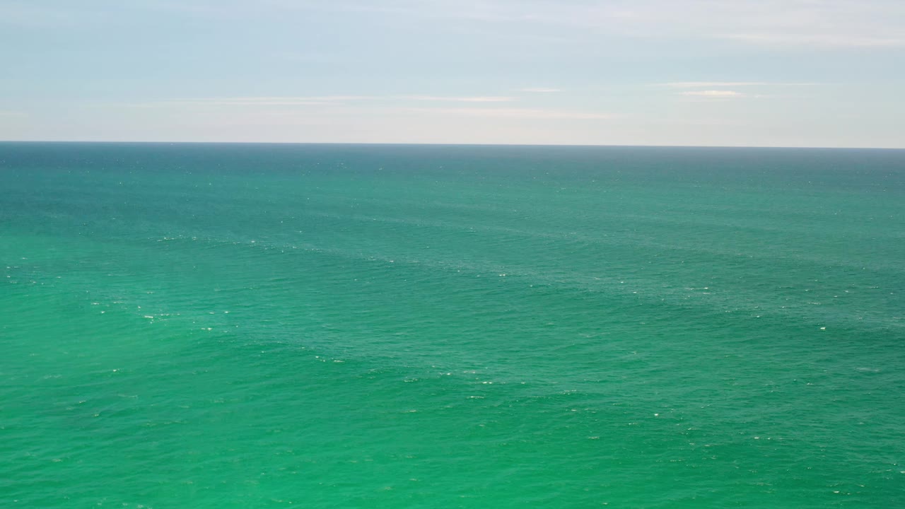 Aerial Los Cabos ocean view with the water surface slightly darker near the horizon, thin cloud bands above, and no visible people or boats.