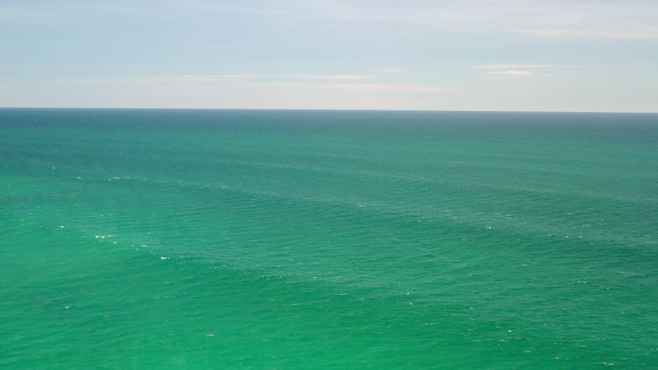 Turquoise-green sea surface below a soft blue sky.