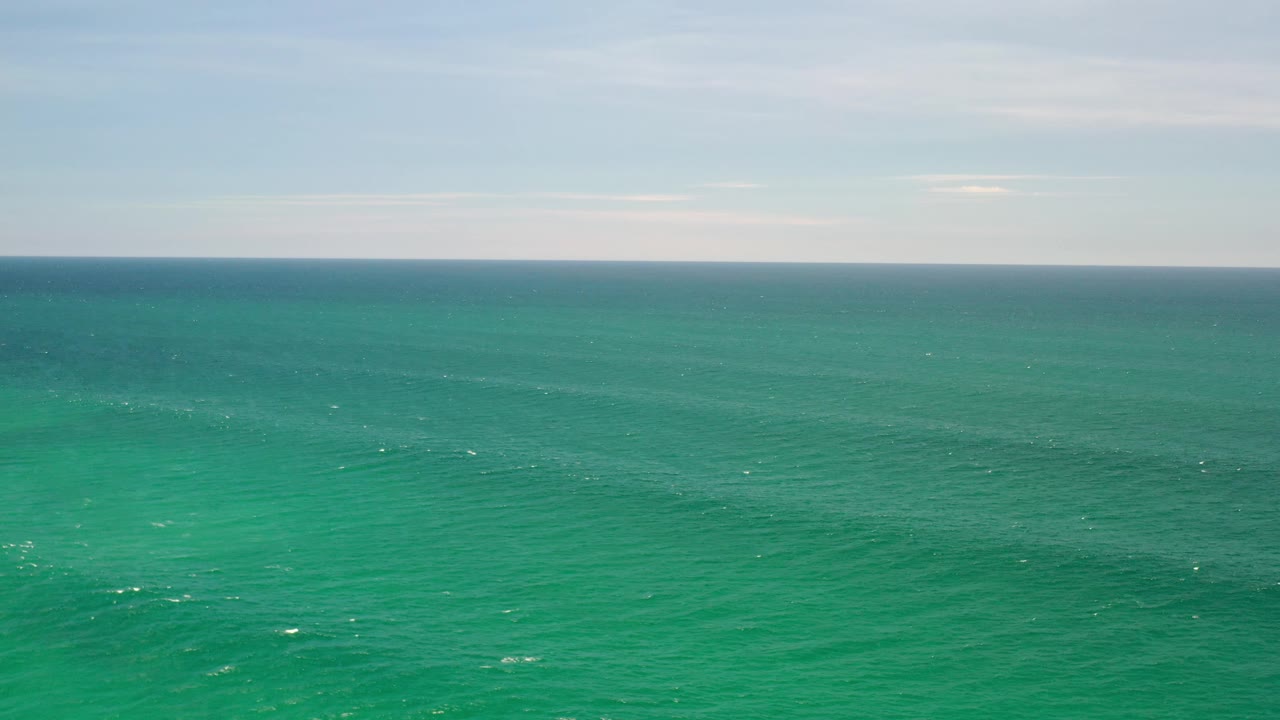 Open ocean with teal water, faint wave lines, and soft clouds above.