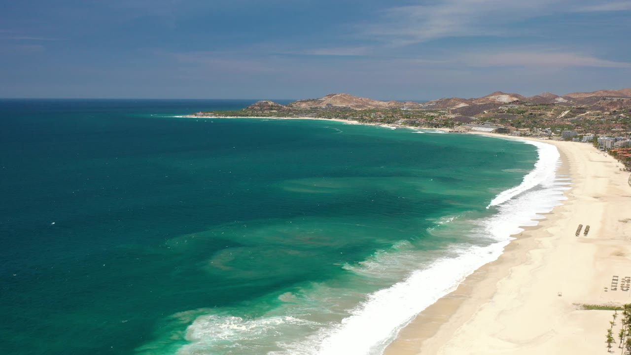 Curving beach and ocean seen from above under clear blue sky