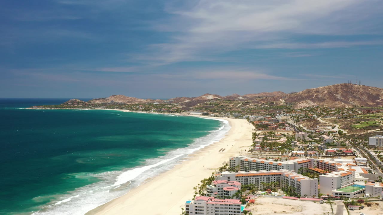 Elevated view of blue water, pale beach, resort rooftops, and arid hills.