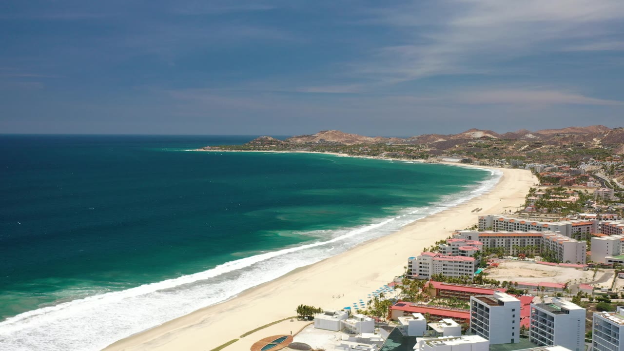 Aerial beach curve with ocean on the left and resort buildings near the shore.