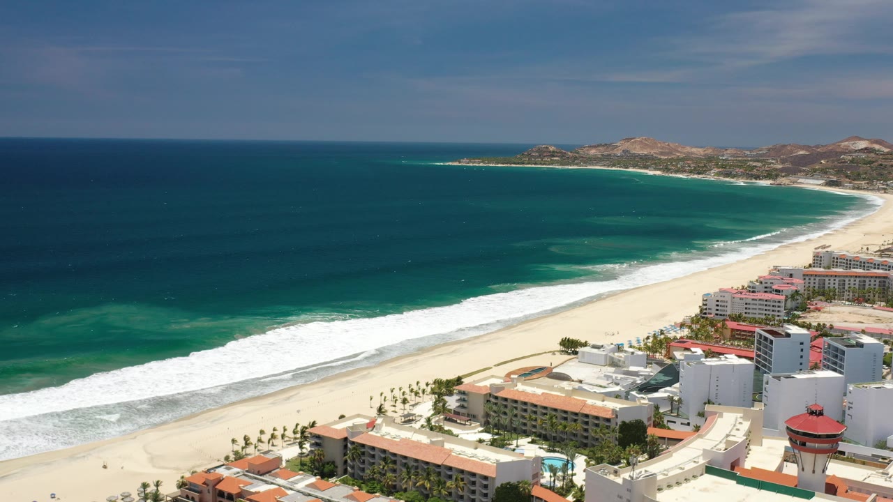 Aerial coastline view with ocean, beach, and buildings at the lower right.