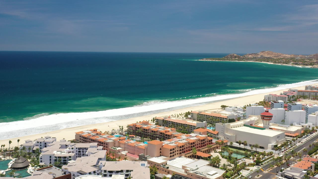 Coastal city buildings beside a curving beach and ocean.