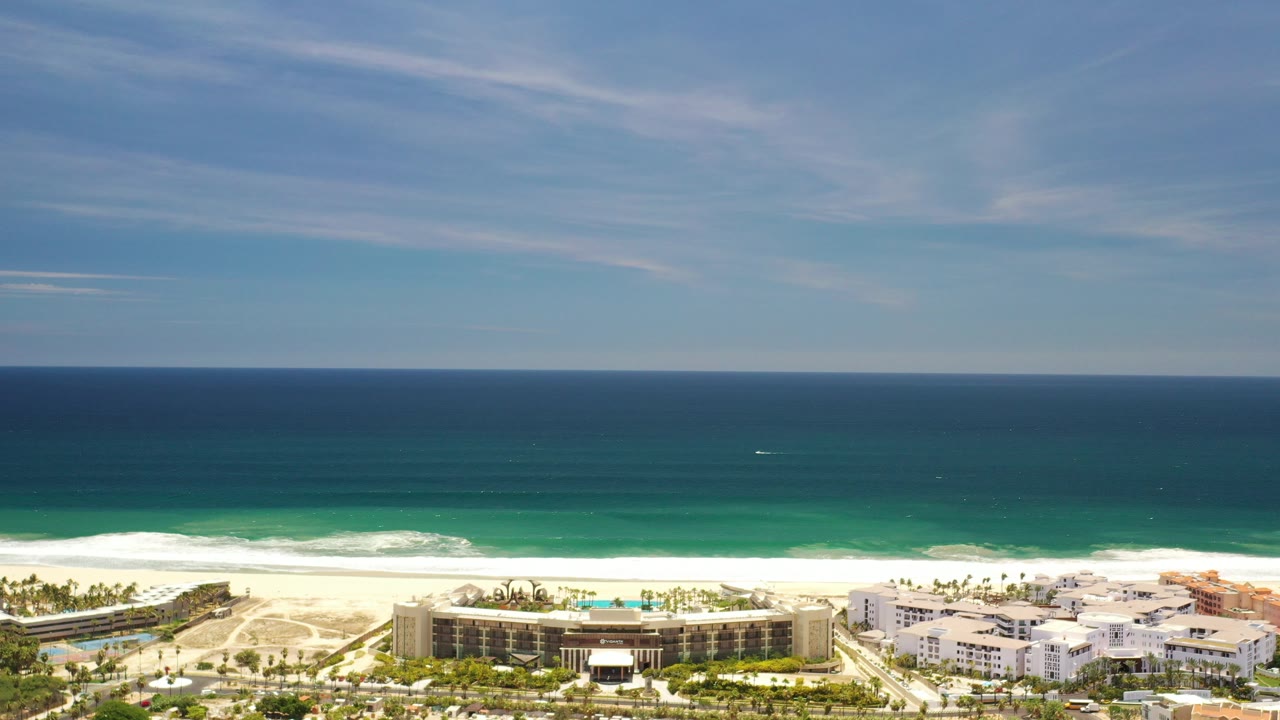 Aerial view of resort buildings beside a sandy beach and blue ocean.