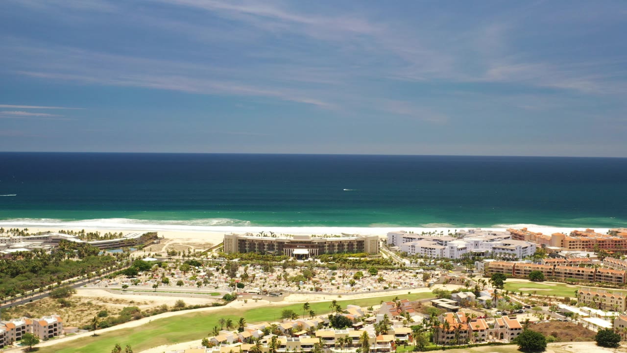 Drone-height view of beachside buildings beside blue ocean.