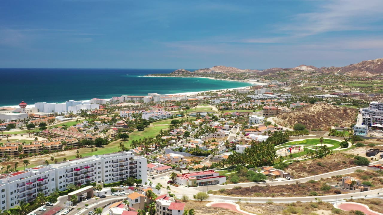 Aerial view of a coastal town with beach, hotels, roads, and mountains.