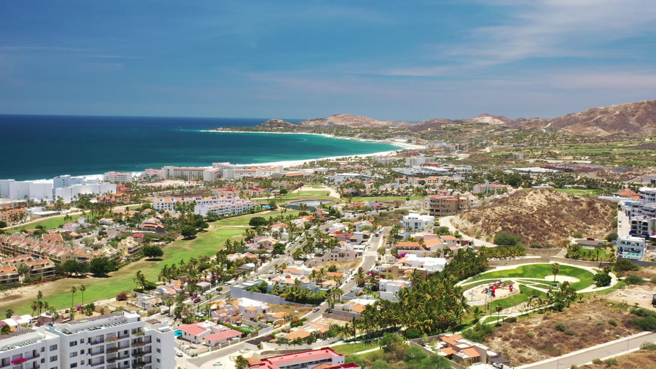 Aerial view of coastal city, golf course, beach, ocean, and hills.