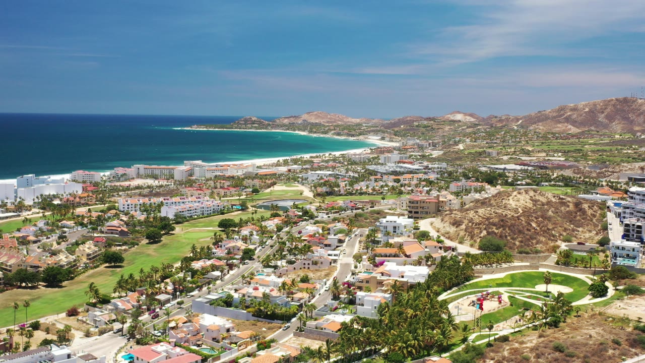 Wide aerial view of coastal town, beach, ocean, golf course, and hills.