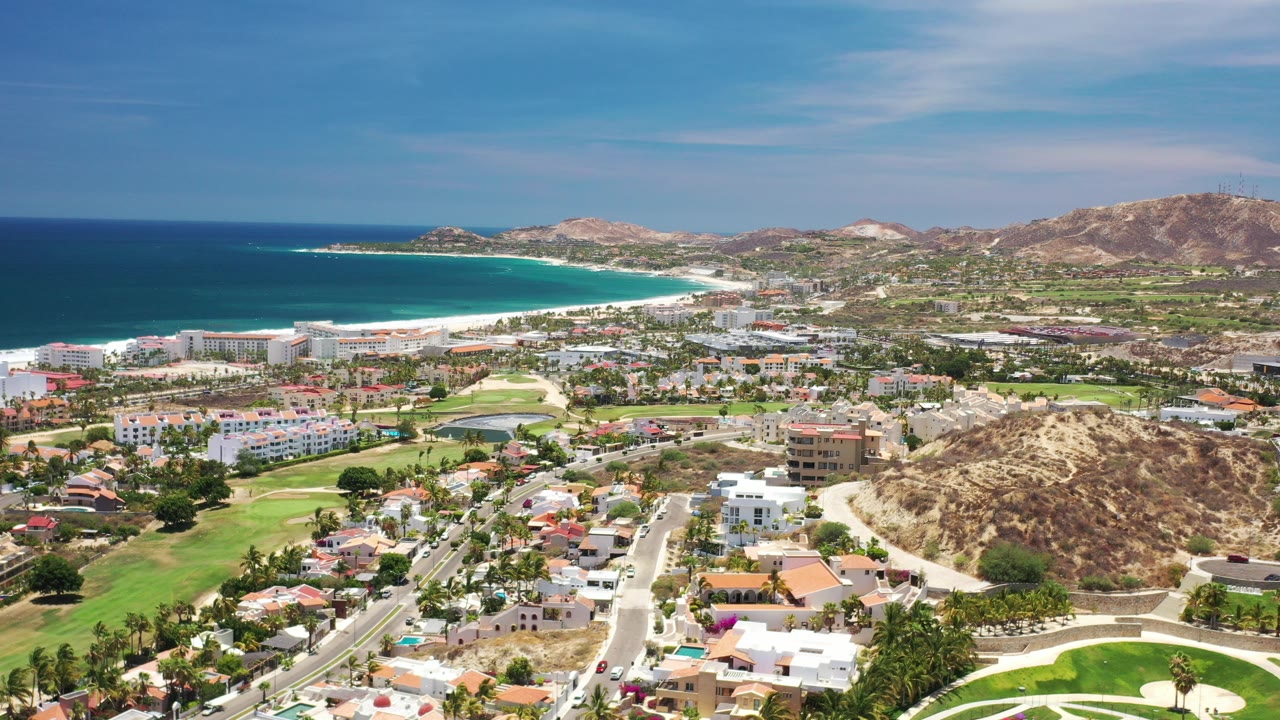 Aerial view of coastal homes, apartments, beach, ocean, and hills.