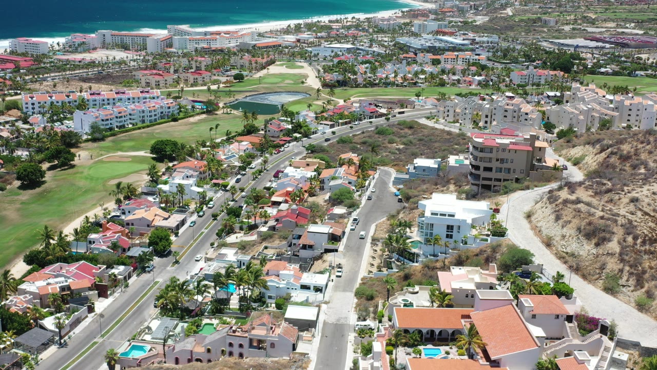Aerial view of hillside homes, roads, golf greens, hotels, beach, and ocean.