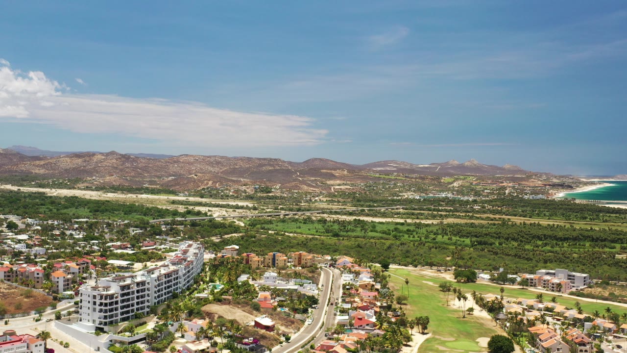 Aerial view of resort buildings, green landscaping, dry hills, and coastline